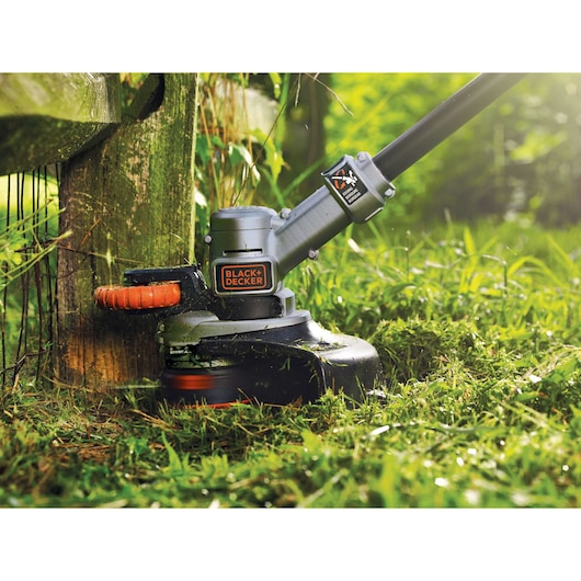 BLACK+DECKER grass trimmer STC1840 in use, close-up view cutting grass near wooden fence outdoors.