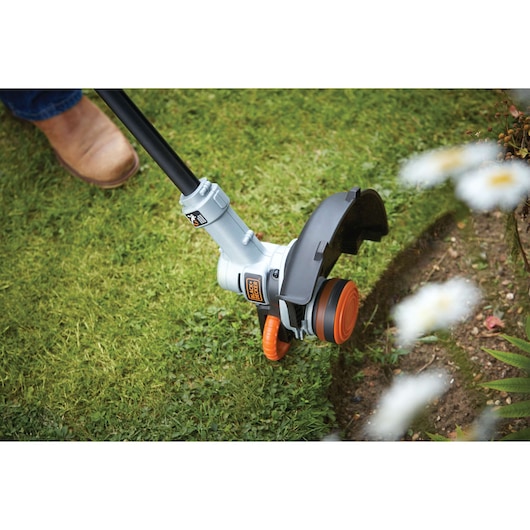 BLACKDECKER STC1840 grass trimmer in use, showing cutting head edging lawn next to flower bed.