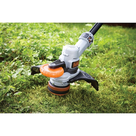 BLACK+DECKER STC1840 grass trimmer in use cutting green grass, close-up of trimming head on lawn.