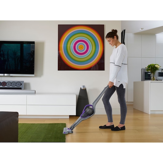 BLACKDECKER SVJ520BFSP stick vacuum in use on green rug and wood floor in modern living room.