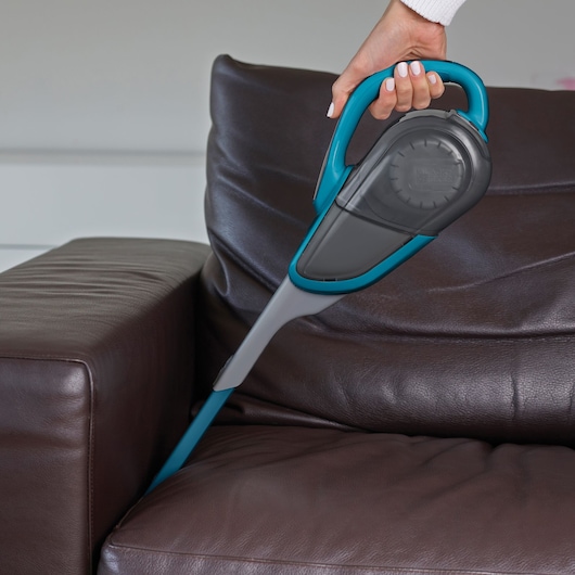BLACKDECKER SVJ520BFS cordless handheld vacuum cleaner with blue and gray design cleaning a brown leather sofa.