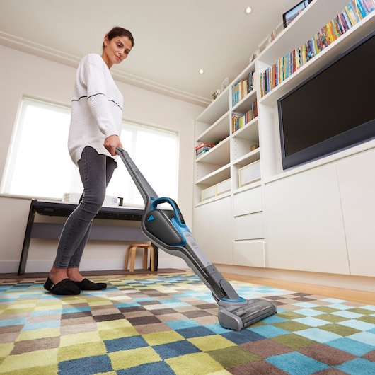 BLACKDECKER SVJ520BFS stick vacuum cleaner used on checkered rug in modern living room.
