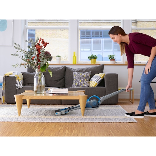 BLACKDECKER SVJ520BFS cordless stick vacuum cleaning under a coffee table in a modern living room.