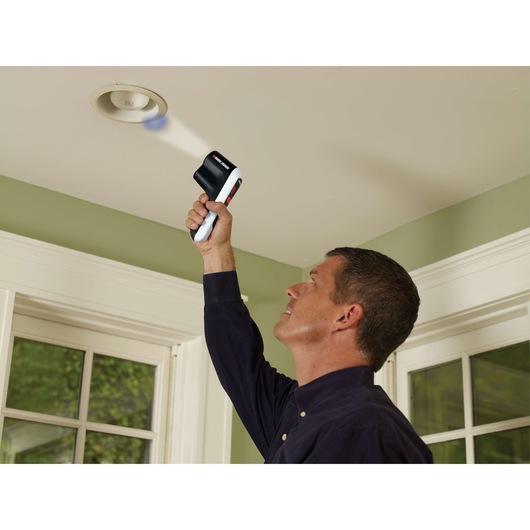 BLACK+DECKER TLD100 thermal leak detector used by a person to check insulation near a ceiling light.