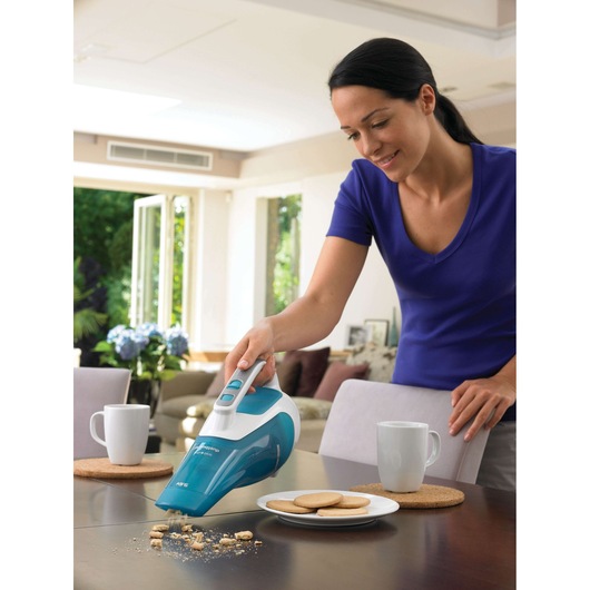 BLACK+DECKER WD9610N handheld vacuum cleaning cookie crumbs from table near white mugs and plate of biscuits.