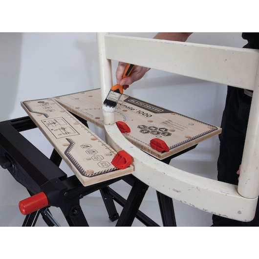 BLACKDECKER WM1000 workbench holding a chair frame with red clamps during painting, photography close-up.