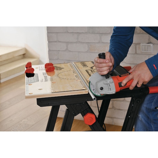 BLACKDECKER WM1000 workbench with red clamps and a person using a power tool to cut a metal pipe, top view.