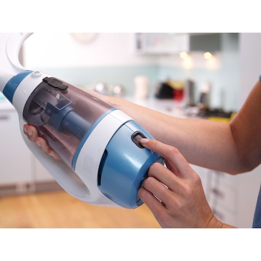 BLACKDECKER WW100 handheld vacuum with blue and white body, user pressing power button in kitchen.