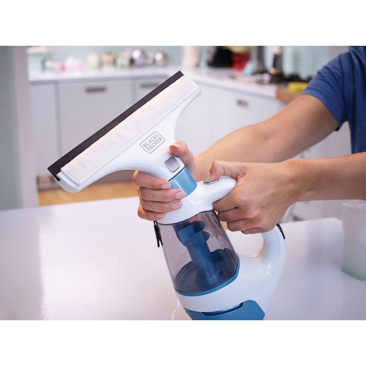 Photo of BLACKDECKER WW100 window vacuum cleaner in use, white and blue, handheld, kitchen background.
